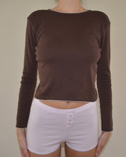 Person wearing a brown long-sleeve top and pink shorts on a plain background