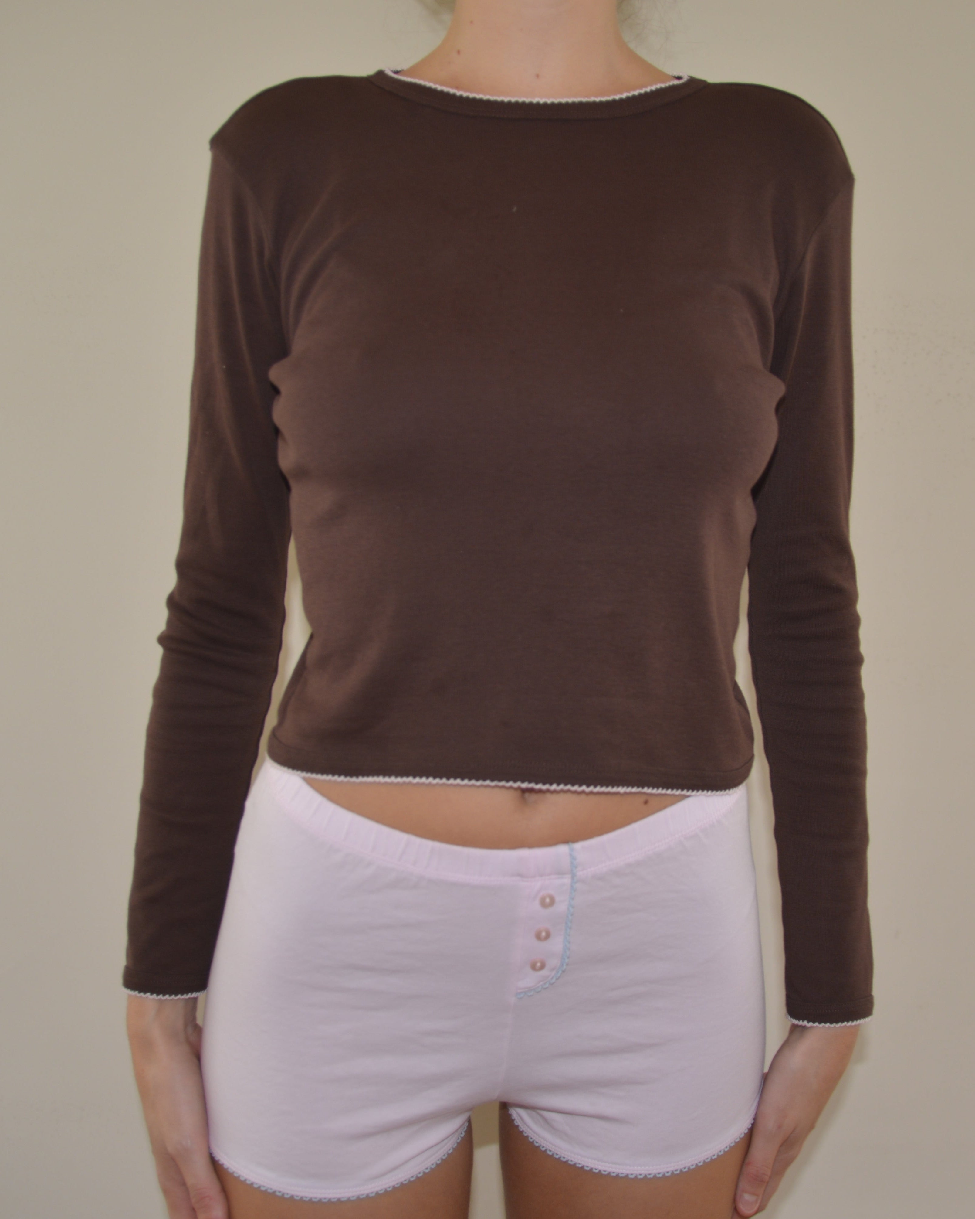 Person wearing a brown long-sleeve top and pink shorts on a plain background